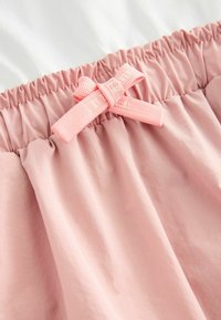 Helle rosa Stoffrock mit einem elastischen Bund, der eine geraffte Textur aufweist, und einer dekorativen rosa Schleife vorne.