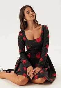 Abito nero con maniche lunghe e scollatura quadrata, decorato con una stampa di rose rosse. Gonna svasata con corpino aderente. Tessuto dalla superficie liscia.