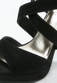 Svart mocka högklackad sandal med korsade remmar och en metallisk silver innersula. Plattformstil med rund tåform.