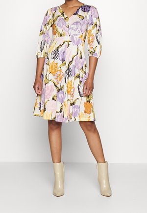 Bloemjurk van witte stof, met paarse, roze en oranje bloemenpatronen. V-hals, driekwart pofmouwen en A-lijn rok.