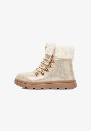 Glittery gold ankle boots with a fluffy white collar, featuring metallic eyelets and matching laces, set on a textured tan sole.