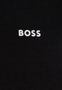 Melna T-krekls ar mīkstu tekstūru, pie kura priekšpuses centrāli izvietots baltais izšūtais logo "BOSS".