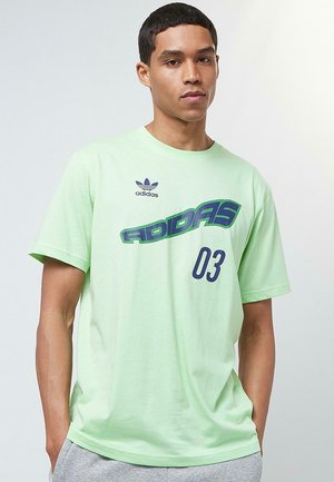 Šviesiai žalia medvilninė marškinėliai su Adidas logotipu ir "ADIDAS 03" tamsiai mėlyna spalva. Trumpomis rankovėmis ir klasikinio apvalaus kaklo dizainas.