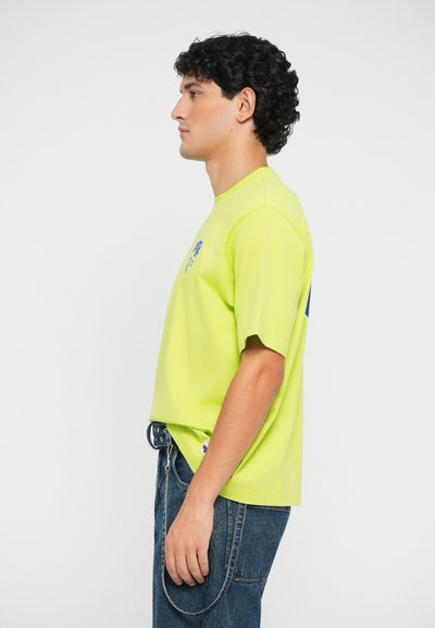 Neon yellow short-sleeve t-shirt with a crew neck, featuring a small blue graphic on the chest and relaxed fit, paired with blue denim jeans.