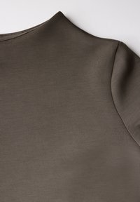 Tessuto marrone, liscio con una leggera lucentezza. La parte superiore ha un collo rotondo e cuciture morbide sulle spalle, enfatizzando un design minimalista.