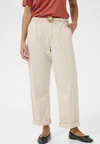 Beiga vida byxor med upplupna cuffs, gjorda av lättviktigt tyg. Stylade med ett flätat bälte och sidfickor. Matchade med svarta ballerina.
