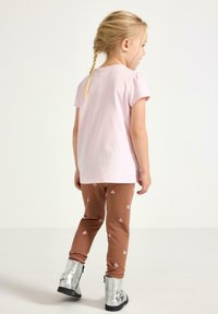 Lyserød bomuld t-shirt med korte ærmer, kombineret med brune leggings med små lyserøde blomsterprint. Båret med sølvfarvede ankelstøvler.