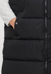 Melnā pūkaina veste ar rāvējslēdzēju, ar faktūru, quiltēta dizaina un sānu kabatām ar noapaļotiem sudraba detaļām.