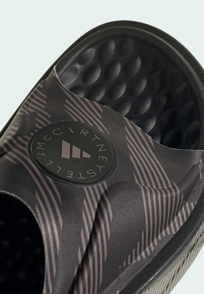 Black slide sandal featuring a textured upper with diagonal stripes, a round logo patch, and a cushioned sole with a honeycomb pattern.