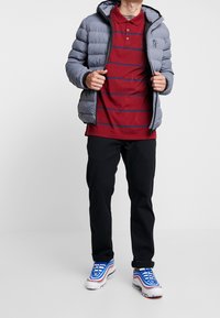 Doudoune grise à capuche, polo rayé rouge, pantalon noir et baskets bleues avec des accents rouges et blancs. Comprend une fermeture éclair à l'avant.