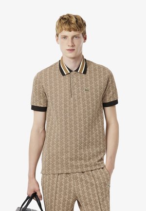 Beige poloshirt met een geometrisch patroon, zwart en gouden gestreepte kraag en korte zwarte mouwen; Lacoste-logo op de borst.