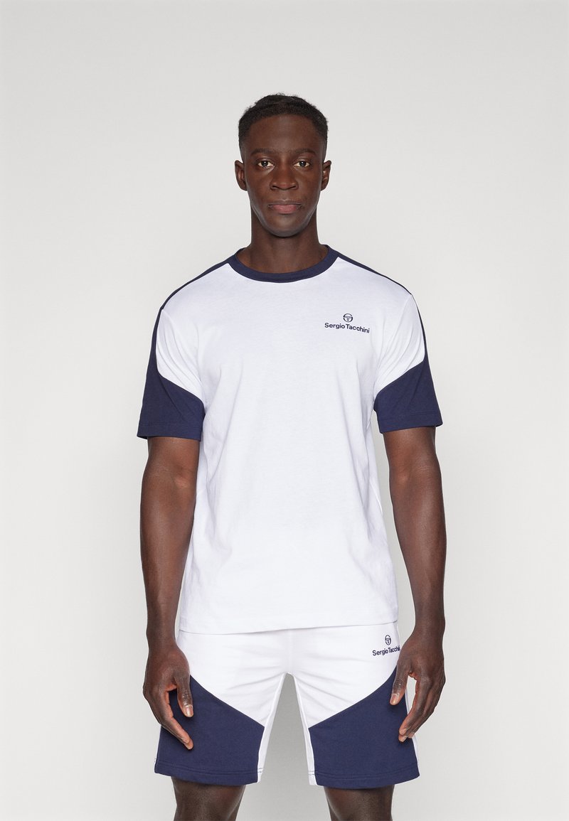 Wit en marineblauw sportt-shirt met korte mouwen, ronde halslijn en logo op de borst, gecombineerd met marineblauwe en witte shorts met schuine accenten.