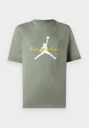 Ελιά πράσινη βαμβακερή T-shirt με στρογγυλή λαιμόκοψη, με λευκό λογότυπο Air Jordan και κίτρινο κείμενο από κάτω. Κοντά μανίκια, χαλαρή εφαρμογή.
