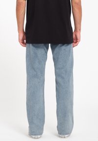 Light blue denim jeans with a relaxed fit and straight leg design, worn with a black cotton t-shirt and white sneakers.