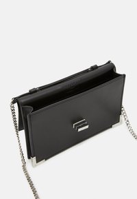 Borsa a tracolla in pelle nera con accessori in tonalità argento, tracolla a catena e chiusura geometrica. Texture liscia, design minimalista e scomparto aperto.