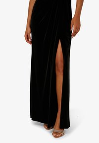 Schwarzes Samtkleid mit einem Seitenschlitz; verfügt über ein drapiertes Design und eine glatte Textur. Abgerundet mit klaren Riemchenabsätzen.