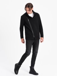 Sort lynlåsjakke med høj krave, parret med slidte sorte jeans og sorte snørebåndsstøvler. Glat stoftekstur og moderne design.