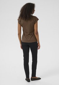 Top corto marrone a maniche corte, aderente in vita, abbinato a pantaloni neri attillati e ballerine nere a trama, visto da dietro.