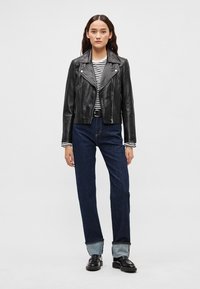 Mustast nahast mootorrattajakk triibulise särgi kohal, mida täiendab tumedast teksast püksid, millel on ülespööratud ääred, ning mustad kingad. Lihtne taust.