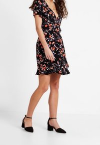 Robe noire à motifs floraux avec de courtes manches à volants, décolleté en V et taille ajustée. Présente des motifs floraux rouges et blancs, longueur au-dessus du genou.