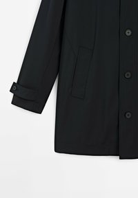 Schwarzer wasserdichter Mantel mit geradem Schnitt, großen Knöpfen, einer seitlichen Tasche und knöpfbaren Manschetten. Glatte Stofftextur.