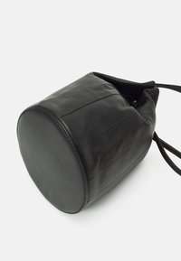 Musta nahkainen säilytyskassi, jossa pyöreä pohja, teksturoitu pinta ja kaksi säädettävää hihnaa, joissa pystysuorat saumauskoristeet.