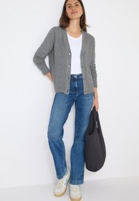 Cardigan grigio a maglia con bottoni, t-shirt bianca, jeans blu, sneakers beige e blu, con una borsa nera. Design semplice e pulito.