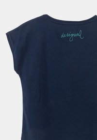 Marinblaues Kurzarmhemd mit einem helltürkisfarbenen, geschwungenen "desigual"-Logo, das nahe dem oberen Rückenkragen gestickt ist.