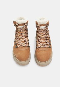 Bottines de randonnée en suède beige avec doublure en fausse fourrure, lacets à motifs marron et beige, et œillets métalliques. Semelles en caoutchouc pour une bonne traction.