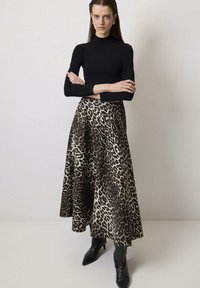 Maglione nero a collo alto abbinato a una gonna fluida con stampa leopardata in beige e nero, completato da stivali neri con punta a cerniera.