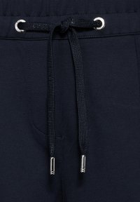 Marineblaue Jogginghosen mit einem Kordelzug mit metallischen Enden, elastischem Bund und einer Seitentasche. Mattes Material mit glatter Textur.