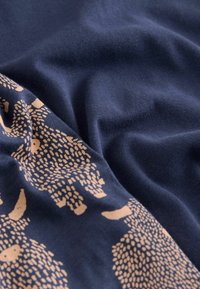 Námořnicko modrá látka s jemnou texturou obsahuje opakující se vzor světle béžových abstraktních tvarů zvířat, což dodává designu detaily.