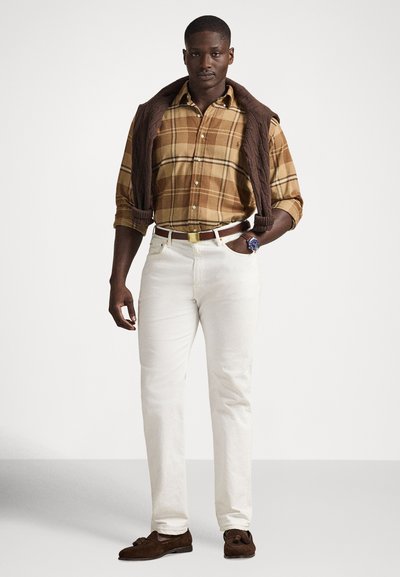 Rjava karo s karirastim vzorcem z dolgimi rokavi, kremasto bele hlače in rjavi zeleni loaferji iz semiša. Rjavi pleteni pulover je premeten čez ramena, z zlatim zaponko na pasu.