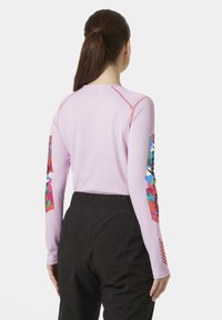 Camiseta ajustada de manga larga en rosa claro con diseños abstractos y coloridos en las mangas. Presenta costuras en contraste y una tela suave y texturizada.