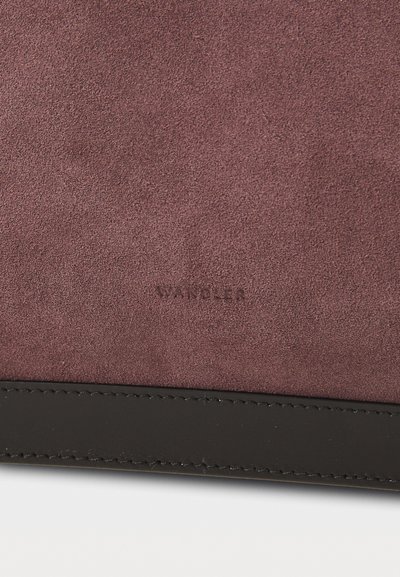 Borsa in suede bordeaux con rifiniture in pelle nera liscia. Presenta un logo inciso in modo discreto vicino alla parte inferiore, enfatizzando la texture e l'artigianato.