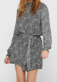 Vestido impreso en blanco y negro con mangas largas, escote fruncido y cintura ceñida con cinturón. La tela tiene un patrón texturizado y moteado.