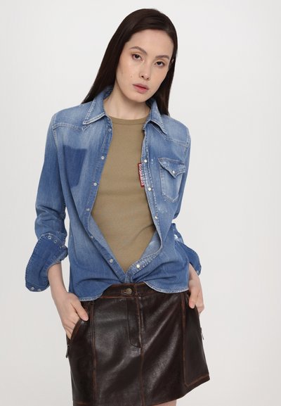 Light blue denim shirt with snap buttons, paired with a fitted olive green top and black leather skirt featuring side pockets and a front button.