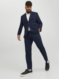 Costum bleu marin cu sacou cu un singur nasture și cămașă albă cu guler. Asortat cu adidași negri cu talpă de culoare crem.