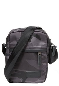 Czarna torba typu crossbody w wzór kamuflażu z zapięciem na zamek, regulowanym paskiem, przednią kieszenią oraz gładką syntetyczną teksturą. Posiada oznaczenie marki.