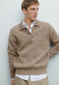 Brauner Strickpullover mit strukturiertem Design, collared Kragen und drei Knöpfen, getragen über einem weißen Hemd, vor einem hellen Hintergrund.