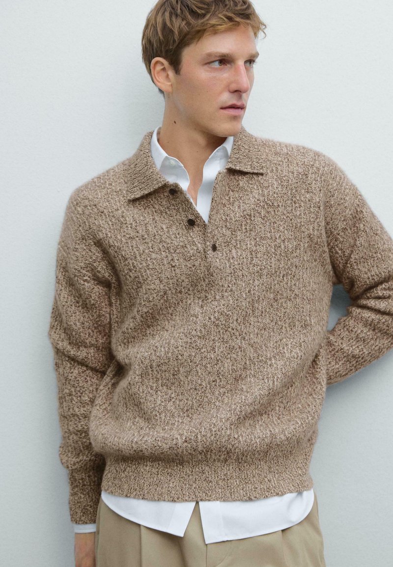 Brauner Strickpullover mit strukturiertem Design, collared Kragen und drei Knöpfen, getragen über einem weißen Hemd, vor einem hellen Hintergrund.