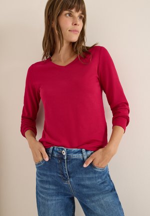 Top aderente a maniche lunghe di un vivace rosa brillante con scollatura a V, abbinato a jeans in denim blu chiaro, con vestibilità comoda e design a cinque tasche.