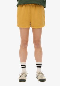 Shorts en coton jaunes avec une taille élastique et un ourlet piqué. Associés à des baskets basses grises et noires et des chaussettes de type crew rayées.