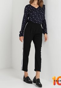 Marineblaue Bluse mit kleinem weißen Blumenmuster, kombiniert mit schwarzen, taillierten Hosen mit weißen Streifen. Schwarze Mokassins runden das Outfit ab.
