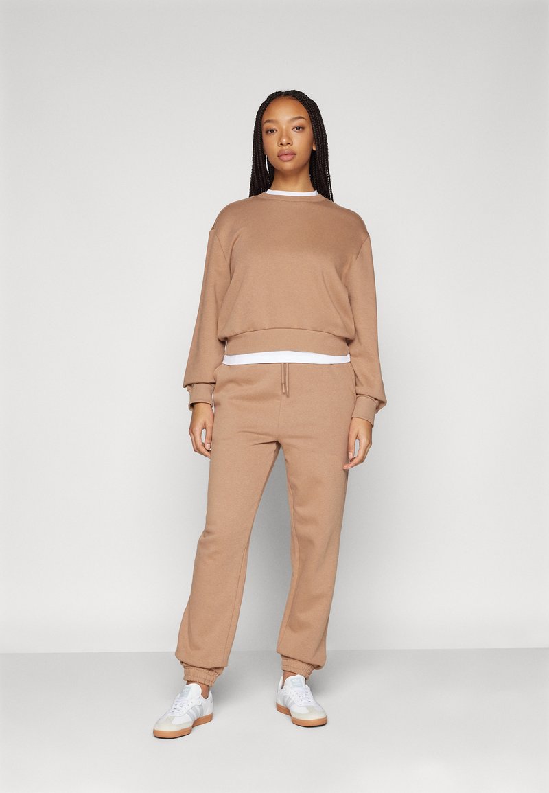 Sudadera cortada marrón con mangas largas y dobladillo acanalado, combinada con joggers a juego que tienen cintura elástica y puños. Zapatillas blancas.