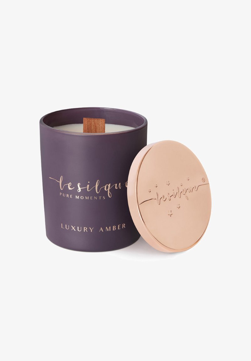 Bougie parfumée ambre de luxe violette avec mèche en bois et couvercle métallique séparé en or rose gravé du nom de la marque.