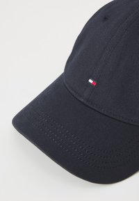 Navy blue baseball cap made of cotton with a curved brim, featuring subtle stitching and a small logo in red, white, and blue at the front.