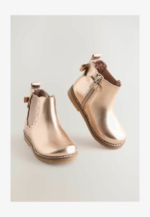 Metalliline roosa kuldne pahkluusaapad sujuva viimistlusega, dekoratiivse sakilise servaga, külje tõmblukuga ja kaunistusega kaar.