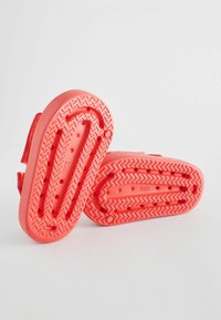 Koralfarvede gummisko med en tekstureret sål. Har en Velcro-rem og en kontureret indersål. Sålens zigzag-mønster giver godt greb.