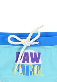 Pantaloni da bagno blu con un corpo azzurro, caratterizzati da una grafica "Paw Patrol" in viola e giallo. Vita con cordoncino e motivo bianco e giallo.